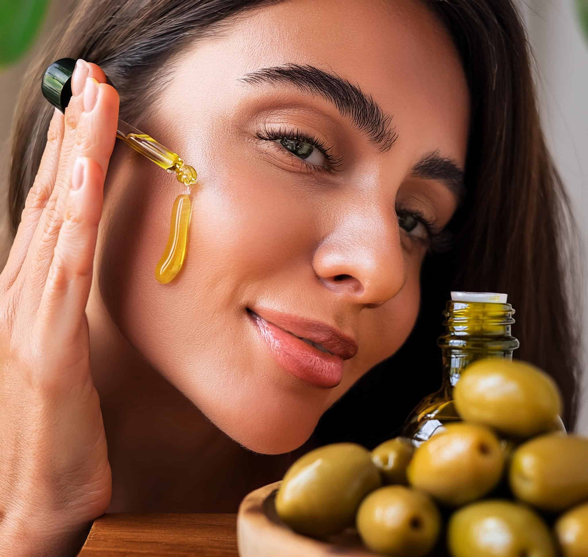 Ženska osoba nanosi maslinovo ulje na lice. Također na slici se nalaze i plodovi maslina.