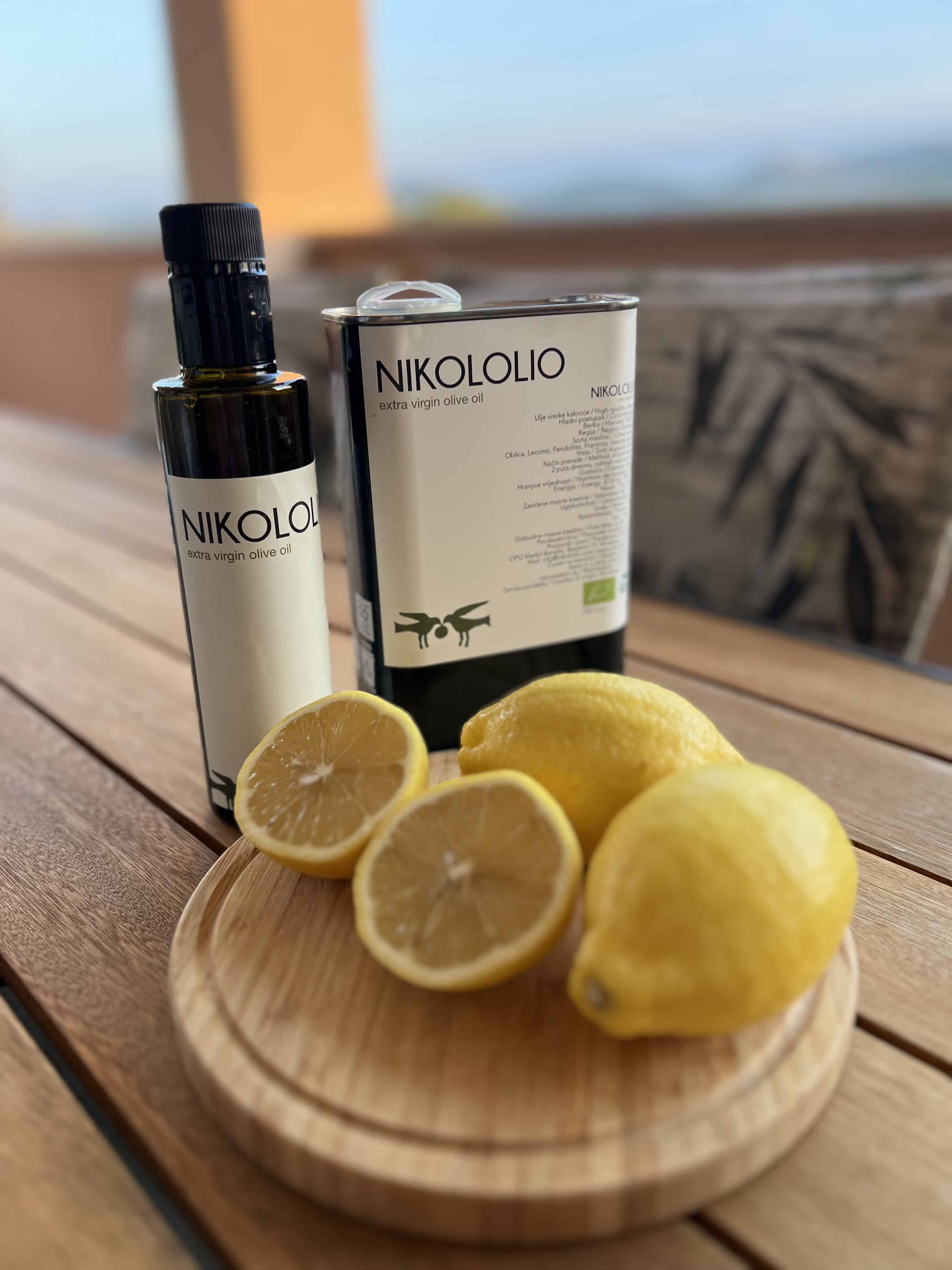 Maslinovo ulje i limun na drvenoj podlozi. Na slici se nalazi 2 cijela limuna i jedan presječen na pola. Također, na slici su dvije boce maslinovog ulja.