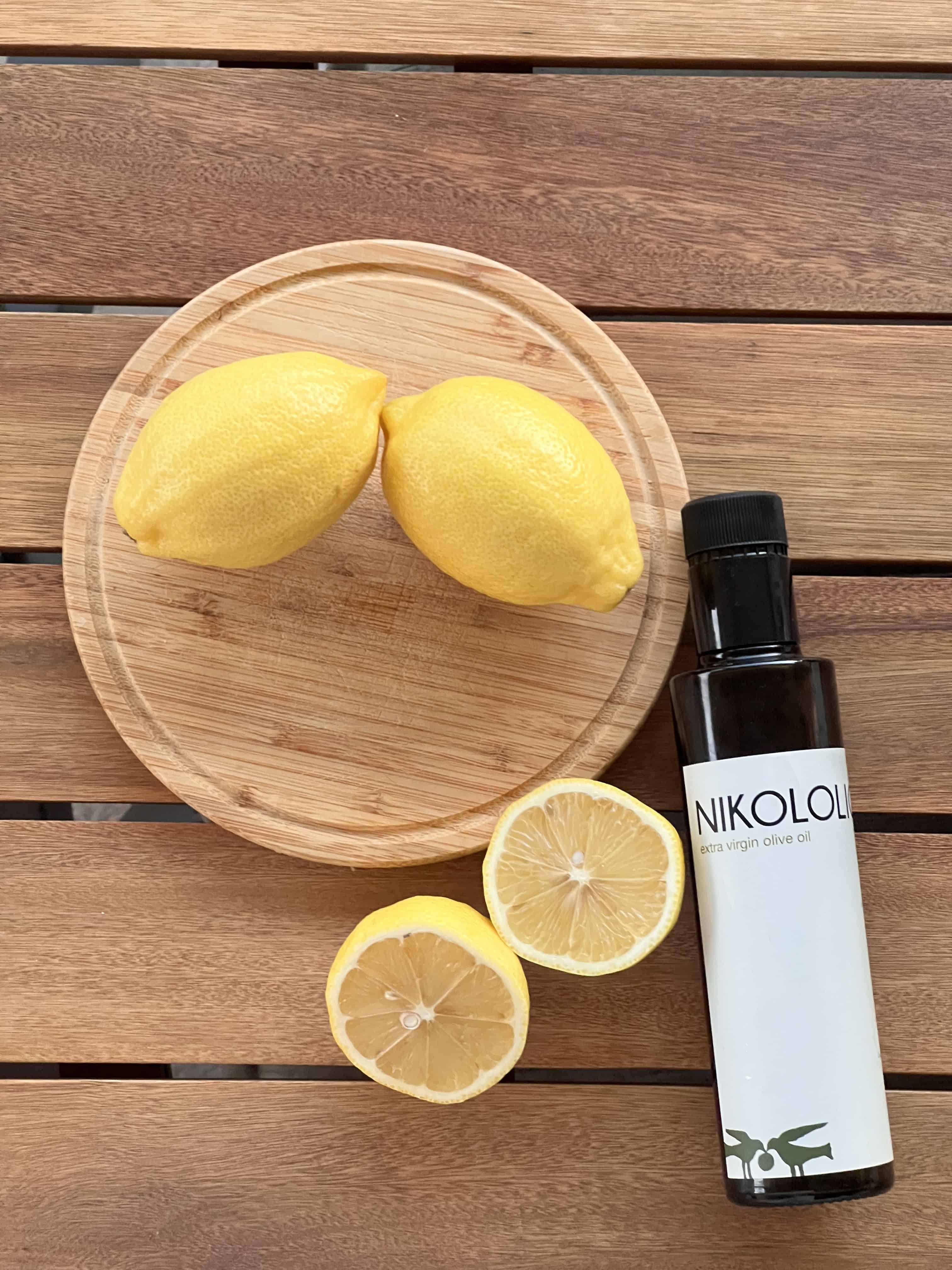 Jedna boca maslinovog ulja i 2 cijela limuna i 1 presječen na pola. Sve skupa se nalazi na drvenoj podlozi.